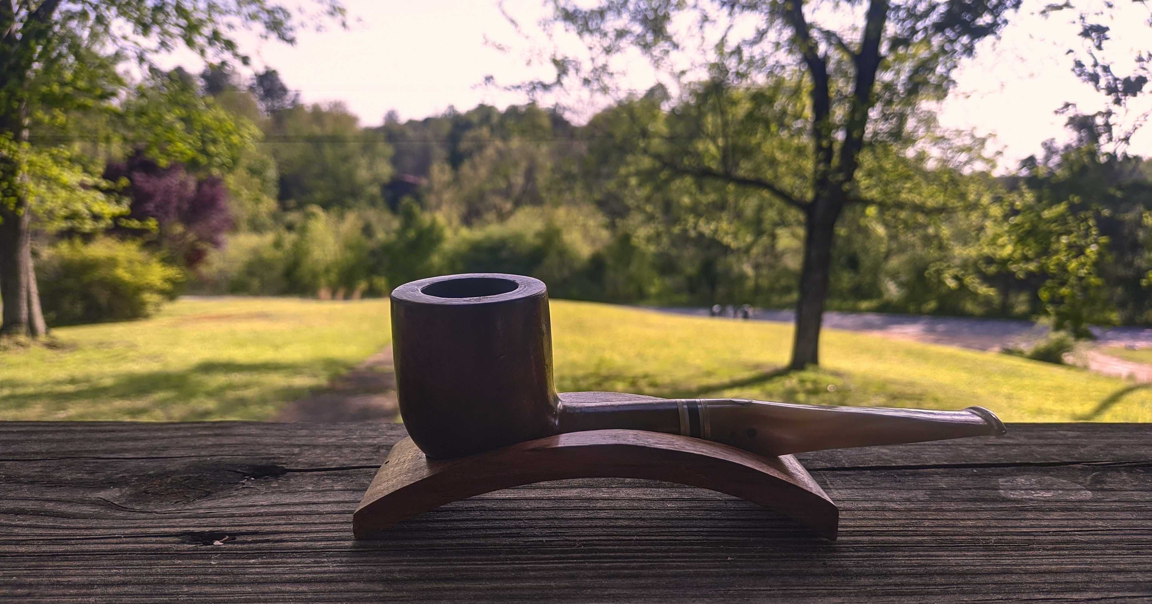 A picture of my pipe from Mauro Armellini. It’s sitting on my porch
rail with the yard in the background; the grass is a light green and the
leaves of the woods further on are darker. The pipe is a rich brown with
a cream-coloured opalescent stem. There is a mother-of-pearl inlay on
top of the stem.