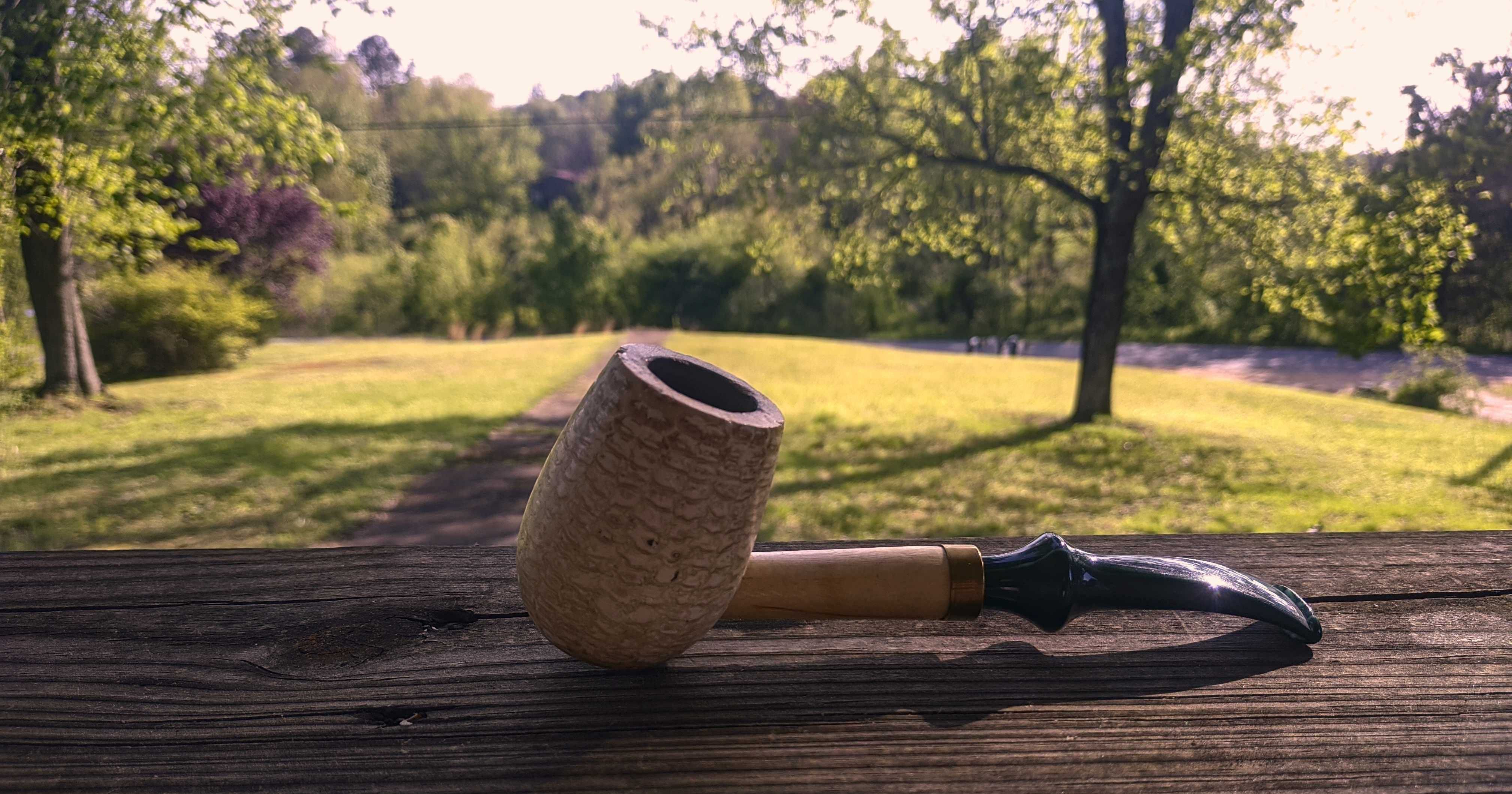 This pipe is a light cream colour. The bowl looks like the cob of anear of corn (that’s what it is) with a short wooden tube sticking out ofit. The bent stem is a deep marbled green.